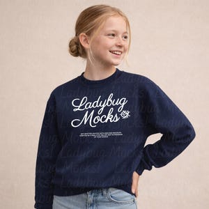 Puede incluir: Una sudadera azul marino con el texto "Ladybug Mocks" en escritura blanca. La sudadera tiene cuello redondo y mangas largas. La modelo lleva vaqueros azules.