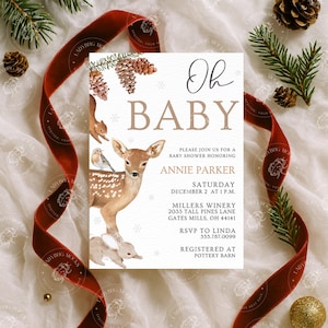 May include: A baby shower invitation with the words "Oh Baby" in elegant script. The invitation features watercolor illustrations of a deer, squirrel, and bunny, with pine cones and snowflakes. A red ribbon and pine branches frame the invitation.