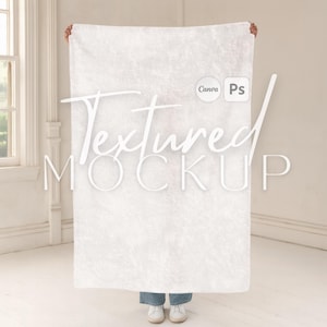 May include: A large, white textured blanket is held up. The blanket has a subtle, mottled pattern. The words "Textured MOCKUP" are written across the blanket in a script font. The background is a light-coloured room with a window.
