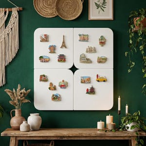 May include: A collection of travel-themed refrigerator magnets, including miniature landmarks like the Eiffel Tower and the Colosseum, displayed on a white magnetic board against a dark green wall. The scene is decorated with plants, candles, and a macrame wall hanging.