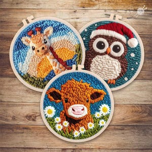May include: Three embroidered hoops featuring animal designs. One depicts a giraffe with a patterned neck, another an owl wearing a Santa hat, and the last a cow surrounded by daisies. Each is set against a blue background.