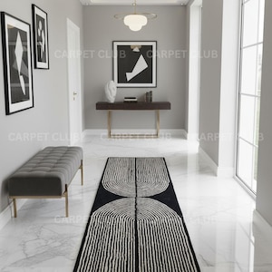 May include: A long rectangular runner rug featuring a black background with a white linear pattern of two mirrored semi-circular arches composed of vertical lines. The rug is positioned on a white marble floor in a hallway with gray walls.