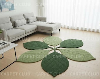 May include: A leaf-shaped rug with six green leaves arranged in a flower pattern. The rug is made of a soft, textured material and is placed on a light-colored wooden floor. The rug is a decorative item for a living room.