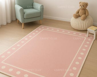 May include: A pink rectangular rug with a white border and large white polka dots. The rug is in a room with a green armchair, framed artwork, and a teddy bear. The rug measures approximately 60 inches by 80 inches.