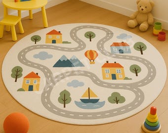 May include: A round, off-white children's rug with a road design, houses, trees, and a sailboat. The rug features a gray road winding through a landscape with a hot air balloon and mountains. A yellow table and chair, a teddy bear, and a toy are nearby.
