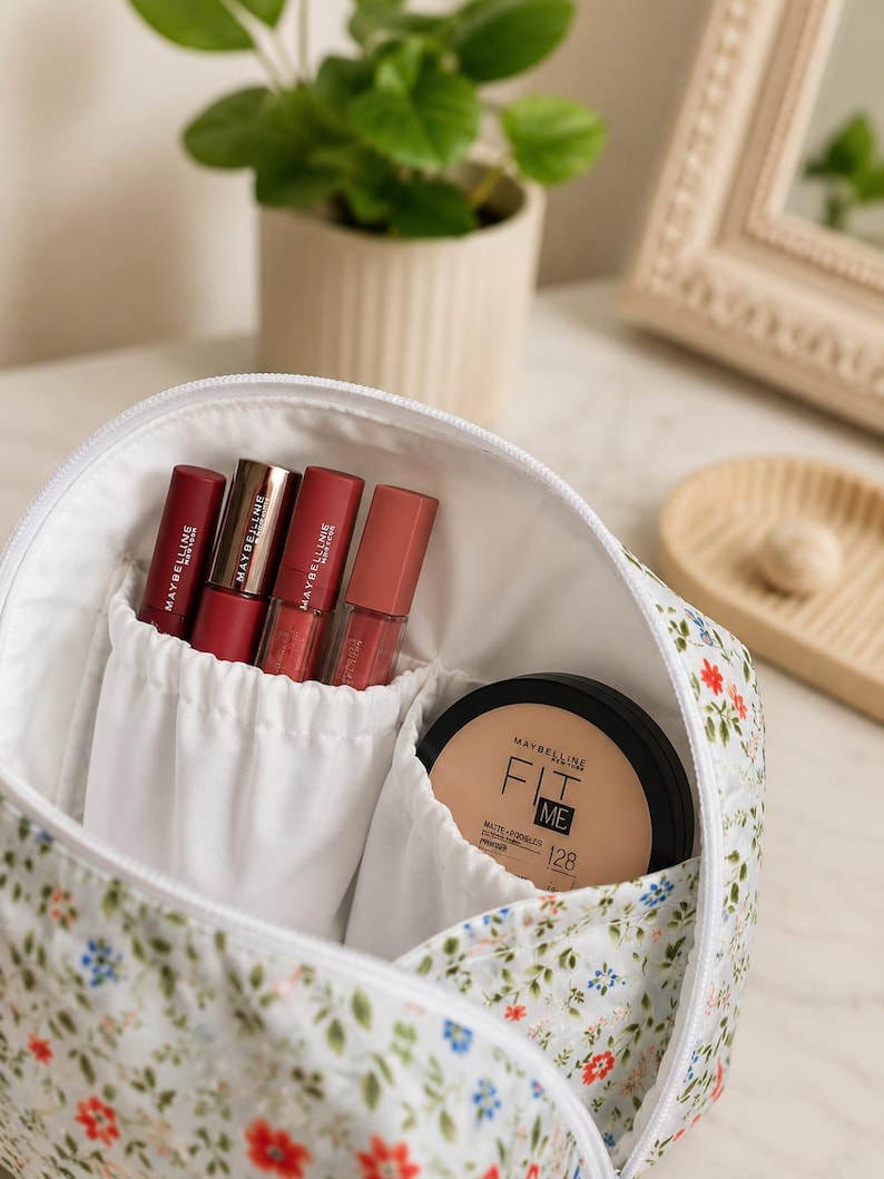 Pu&ograve; includere: Una trousse bianca con motivo floreale di piccoli fiori rossi e blu e foglie verdi. All'interno si trovano quattro prodotti per labbra Maybelline e una cipria compatta opaca Maybelline Fit Me nella tonalit&agrave; 128, in tasche bianche.