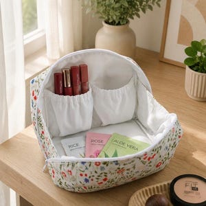 Pu&ograve; includere: Una borsa cosmetica bianca con un colorato motivo floreale con fiori rossi, blu e verdi. L'interno presenta tasche in tessuto bianco contenenti tre rossetti rossi e tre bustine piatte per la cura della pelle etichettate Rice, Rose e Aloe Vera.