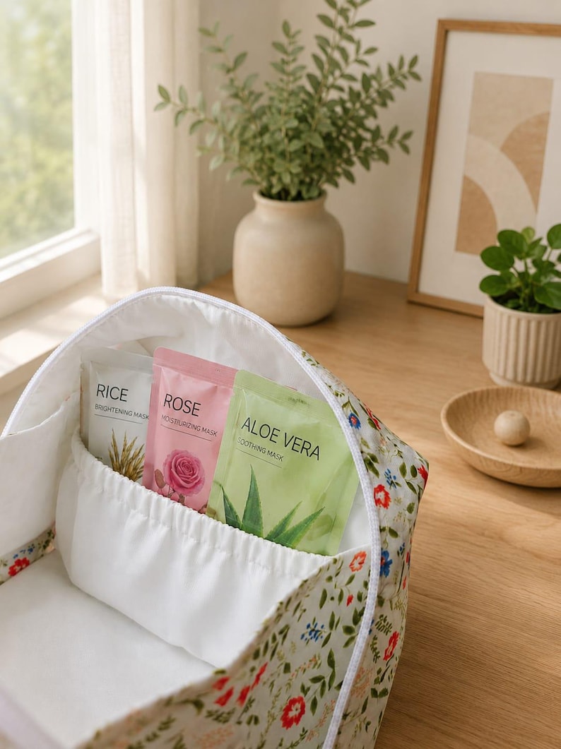 Pu&ograve; includere: Una borsa cosmetica in tessuto bianco con motivo floreale contenente tre maschere per il viso. Le maschere sono etichettate come Rice Brightening Mask, Rose Moisturizing Mask e Aloe Vera Soothing Mask, ognuna con illustrazioni botaniche.