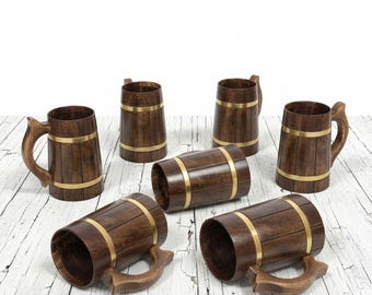 Könnte beinhalten: Sechs Bierkrüge aus Holz mit Messingbändern. Die Krüge haben eine dunkelbraune Oberfläche und gebogene Griffe. Die Krüge sind auf einer weißen Holzoberfläche angeordnet.