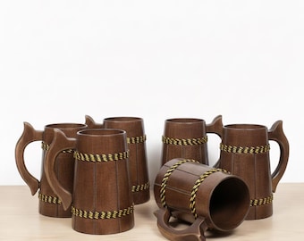 Könnte beinhalten: Sechs Bierkrüge aus Holz mit dunkelbraunen Oberflächen und dekorativen Seilakzenten. Jeder Krug hat einen Griff und eine zylindrische Form. Die Krüge sind auf einer hellen Holzoberfläche vor einem weißen Hintergrund angeordnet.
