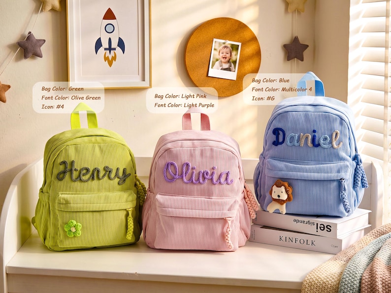 Op de afbeelding: Drie rugzakken van corduroy in groen, lichtroze en blauw. De groene tas heeft de naam Henry in olijfgroen met een bloemicoon. De lichtroze tas toont de naam Olivia in paars. De blauwe tas toont de naam Daniel in meerkleurige letters.
