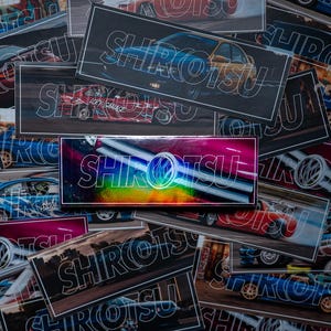 May include: A pile of rectangular stickers displaying car designs and the word "SHIROTSU" in a white outline. The stickers feature diverse car colours and styles, with a holographic sticker at the centre.