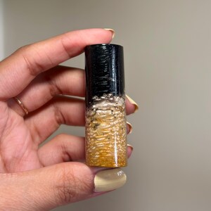 May include: A cylindrical object with a black top, a speckled tan and white middle section, and a tan bottom. The object is held in a hand.
