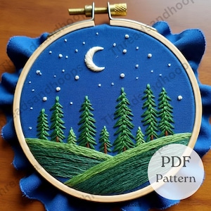 May include: An embroidered hoop art piece featuring a night scene. The design includes a crescent moon, stars, and evergreen trees on a dark blue background. The text "PDF Pattern" is visible. The embroidery is set in a wooden hoop.