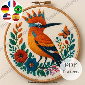 May include: Embroidered hoop art featuring a vibrant bird with orange, blue, and yellow plumage, surrounded by colorful flowers and foliage. The design includes a butterfly and is set against a cream-colored background. The text "PDF Pattern" is visible.