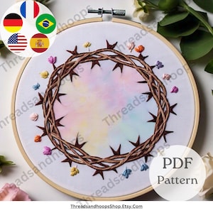 Op de afbeelding: Geborduurde hoepelkunst met een bruine doornenkroon en donkerbruine doornen. De achtergrond is een aquarel wassing van pastelkleuren. Kleine, kleurrijke geborduurde bloemen zijn rond de kroon verspreid. De tekst "PDF Pattern" is zichtbaar.