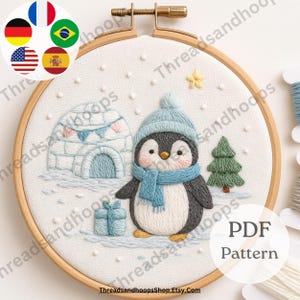 May include: Embroidered hoop art featuring a cute penguin in a winter scene. The penguin wears a blue hat and scarf, standing near an igloo, a gift, and a Christmas tree. The text "PDF Pattern" is visible.
