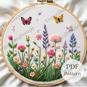 May include: Embroidered floral design in a wooden hoop. The artwork features a variety of colorful flowers, green leaves, and butterflies in shades of pink, purple, yellow, and white. The text "PDF Pattern" is visible.