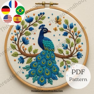 May include: An embroidered peacock design in a wooden hoop. The peacock has blue and teal feathers, with blue flowers and green leaves on the branch. The text "PDF Pattern" is visible. The design is set against a cream background.