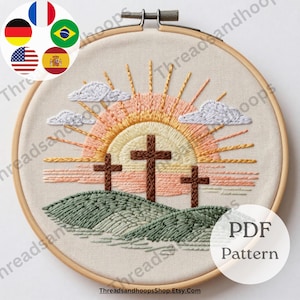 May include: Embroidered hoop art depicting three crosses on a hill, with a sunrise and clouds. The design uses shades of brown, peach, and green. The text "PDF Pattern" is visible. The Etsy shop name "ThreadsandhoopsShop.Etsy.com" is also visible.