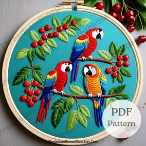 May include: Embroidered artwork featuring three colorful parrots perched on a branch with red cherries and green leaves. The parrots have red, yellow, blue, and white plumage. The design is set against a teal background within a wooden embroidery hoop. The text "PDF Pattern" is visible.