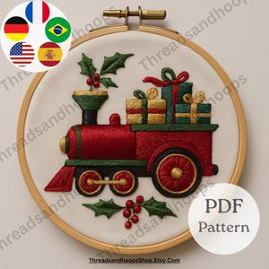 Op de afbeelding: Geborduurd kersttreindesign in een houten hoepel. De trein is rood met groene en gouden accenten, met verpakte cadeaus. Hulst en bessen zijn ook geborduurd. De tekst "PDF Pattern" is zichtbaar.
