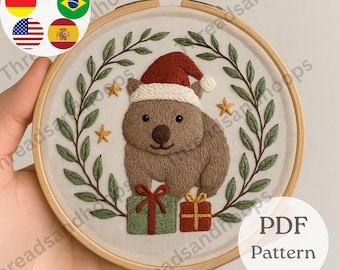 May include: Embroidered Christmas wombat wearing a Santa hat, surrounded by green leaves and gold stars. Two wrapped gifts are at the bottom. The design is in a wooden embroidery hoop. The text "PDF Pattern" is visible.