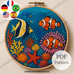 Op de afbeelding: Geborduurde hoepelkunst met een onderwaterscène met kleurrijk koraal, zeesterren en vissen. Het ontwerp bevat een geel-zwart gestreepte vis, clownvissen en de tekst "PDF Pattern". De achtergrond is diepblauw.