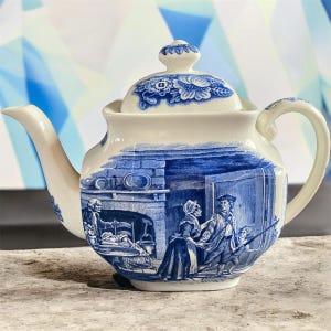 May include: A white and blue ceramic teapot with a lid. The teapot features a blue transferware design depicting a historical scene. The spout and handle are white. The lid has a floral pattern. A classic piece for tea lovers.