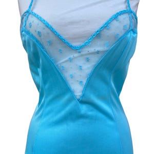 Pu&ograve; includere: Un abito da notte in raso blu turchese con un pannello di pizzo trasparente sul d&eacute;collet&eacute;. Il pizzo presenta un piccolo motivo floreale.