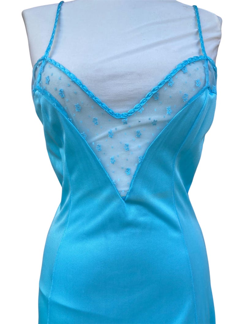 Pu&ograve; includere: Un abito da notte in raso blu turchese con un pannello di pizzo trasparente sul d&eacute;collet&eacute;. Il pizzo presenta un piccolo motivo floreale.