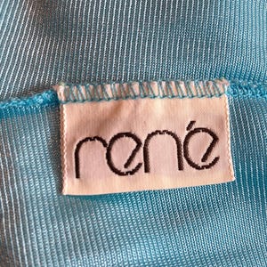 Pu&ograve; includere: Un primo piano di un'etichetta in tessuto blu chiaro con la parola "ren&eacute;" stampata in nero.