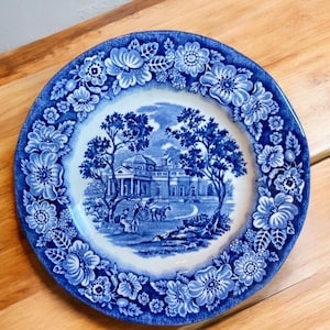 May include: Blue and white ceramic plate with a floral border and a central image of a historic building with trees and a carriage.