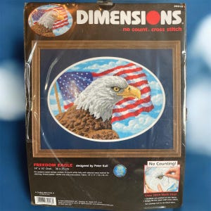 Op de afbeelding: Een Dimensions kruissteekpakket met een Amerikaanse zeearend en de Amerikaanse vlag. De kit heet "Freedom Eagle" en meet 36 x 25 cm (14 x 10 inch). De verpakking bevat de tekst "no count. cross stitch".
