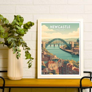 May include: A framed art print featuring a stylized illustration of Newcastle, England. The image showcases the iconic bridge over a river, with buildings and a blue sky. The text "NEWCASTLE ENGLAND" is at the top of the print.
