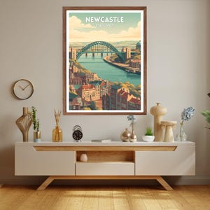 May include: A framed art print featuring a stylized illustration of Newcastle, England. The artwork depicts a green arch bridge over a river, with buildings and a blue sky. The text "Newcastle England" is at the top.