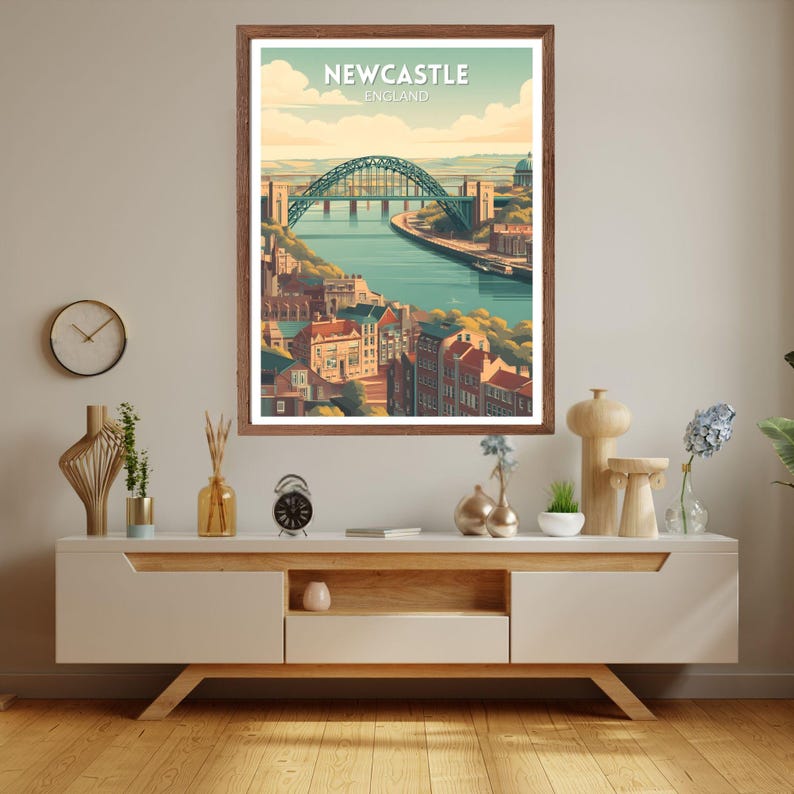 May include: A framed art print featuring a stylized illustration of Newcastle, England. The artwork depicts a green arch bridge over a river, with buildings and a blue sky. The text "Newcastle England" is at the top.