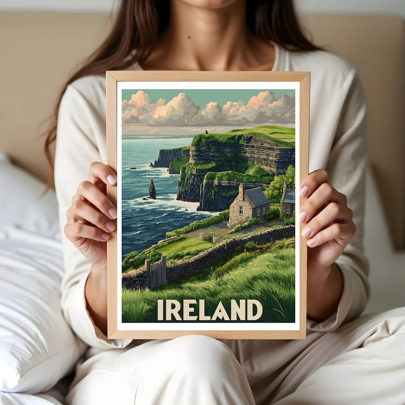 K&ouml;nnte beinhalten: Ein gerahmter Druck mit einer malerischen Ansicht der irischen K&uuml;ste. Das Kunstwerk zeigt gr&uuml;ne Klippen, ein Steinh&auml;uschen und das Wort "IRELAND" in wei&szlig;en Buchstaben. Der Druck wird von einer Person gehalten.