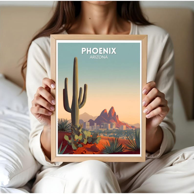 May include: A framed art print featuring a stylized landscape of Phoenix, Arizona. The artwork depicts a large saguaro cactus, desert plants, and the city skyline against a sunset sky. The text "PHOENIX ARIZONA" is at the top.