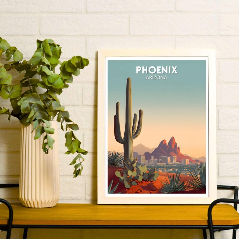 May include: A framed art print featuring a desert landscape with a large saguaro cactus, mountains, and the city skyline of Phoenix, Arizona. The print has a white border and the text "PHOENIX ARIZONA" at the top.