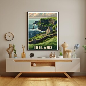 K&ouml;nnte beinhalten: Ein gerahmter Druck der irischen K&uuml;ste mit gr&uuml;nen Klippen, einem Steinh&auml;uschen und dem Wort "IRELAND" in Wei&szlig;. Das Kunstwerk hat eine Vintage-Reiseplakat-&Auml;sthetik und zeigt Meer und Himmel.