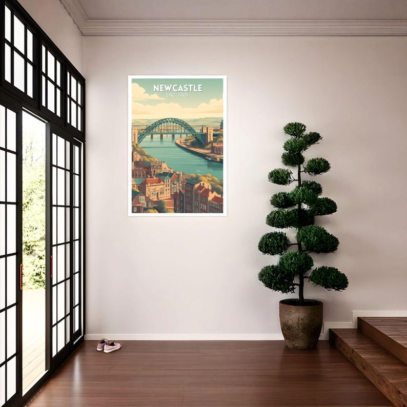 May include: A framed art print of Newcastle, England, featuring a teal bridge over a river, with buildings along the banks. The print has a white border and the text "Newcastle England" at the top. The artwork is displayed in a room with a large window and a potted plant.