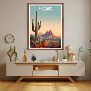 May include: A framed art print featuring a desert landscape with a large saguaro cactus, mountains, and a city skyline. The print has the text "PHOENIX ARIZONA" at the top. The color palette includes shades of green, orange, and blue.