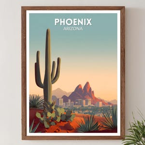 May include: Framed art print featuring a desert landscape with a large cactus in the foreground. The print displays the city of Phoenix, Arizona, with the city name at the top. The color palette includes shades of orange, blue, and green.