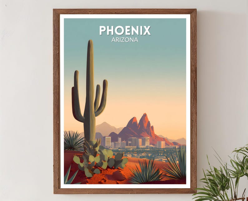 May include: Framed art print featuring a desert landscape with a large cactus in the foreground. The print displays the city of Phoenix, Arizona, with the city name at the top. The color palette includes shades of orange, blue, and green.
