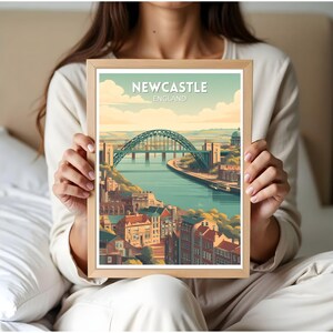 May include: A framed art print featuring a stylized illustration of Newcastle, England. The print showcases the Tyne Bridge over a river, with buildings and a blue sky. The text "Newcastle England" is at the top.