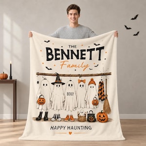 May include: A cream-colored fleece blanket featuring a Halloween-themed graphic with five ghosts hanging from a branch. The text reads THE BENNETT Family, BOO!, and HAPPY HAUNTING. The design includes pumpkins, a witch hat, a broom, and bats.