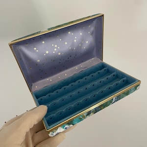 May include: A vintage jewelry box with a blue and green marbled design and gold trim. The inside is lined with blue velvet and has multiple compartments for storing jewelry.