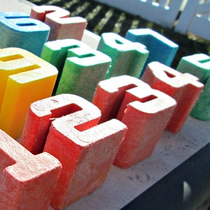 May include: A set of colorful wooden blocks with numbers painted on them. The blocks are arranged in a row, with the numbers 1, 2, 3, 4, 5, 6, 7, 8, 9, 10, 11, 12, 13, 14, 15, 16, 17, 18, 19, 20, 21, 22, 23, 24, and 25 visible.