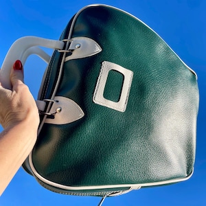 May include: Green and white handbag with a white handle. The bag has a rectangular white accent and white trim. The bag is held against a bright blue sky.